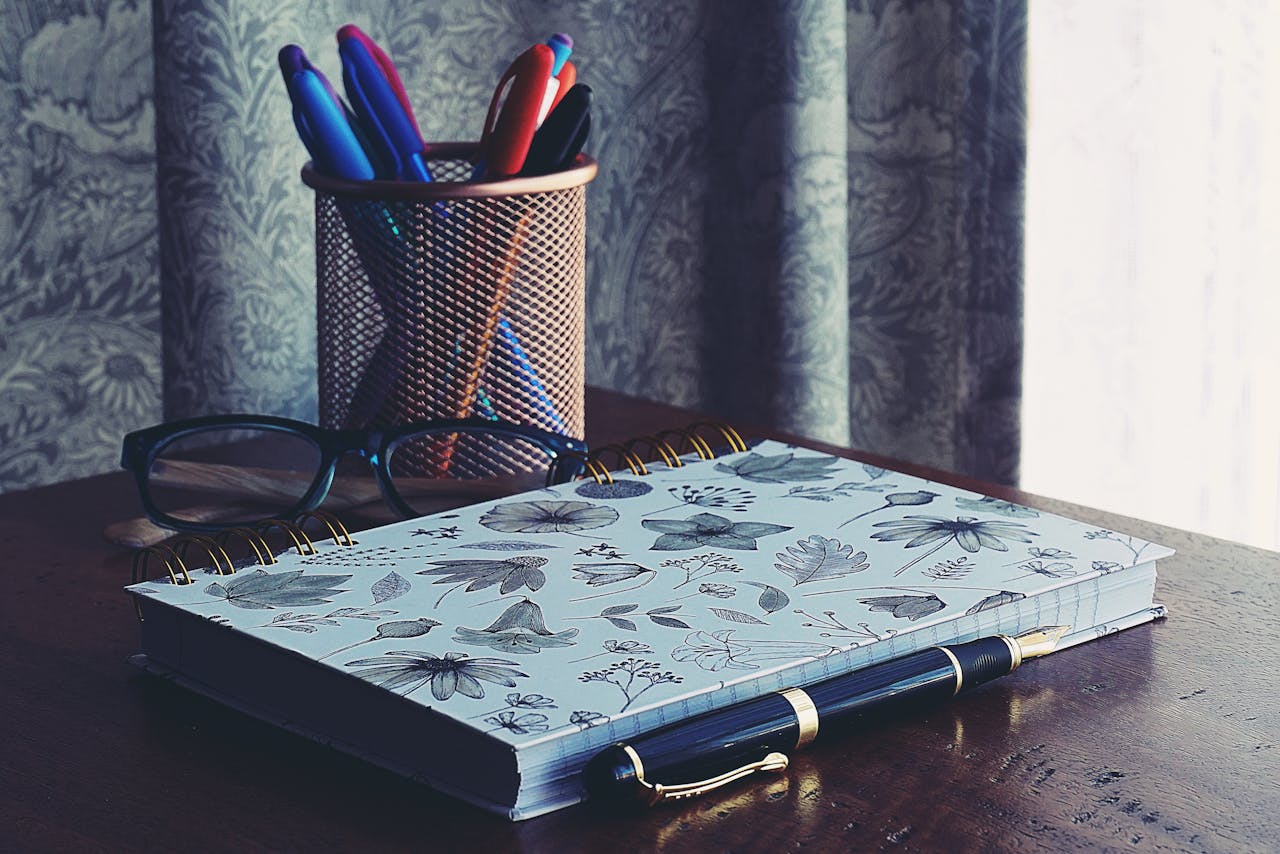 Close-Up Photography of Notebook Near Pens
