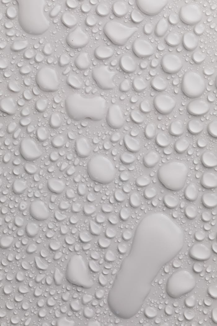 Water texture wet background of light gray color with transparent water drops of different sizes and shapes flowing down together